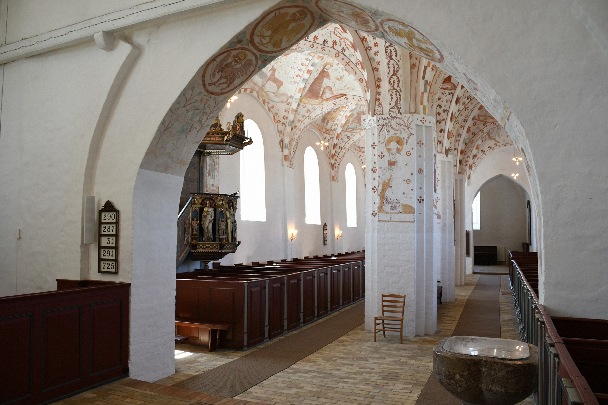 Innenraum der Fanefjord Kirke mit romanischen Bögen, mittelalterlichen Wandmalereien und geschnitztem Altarretabel.