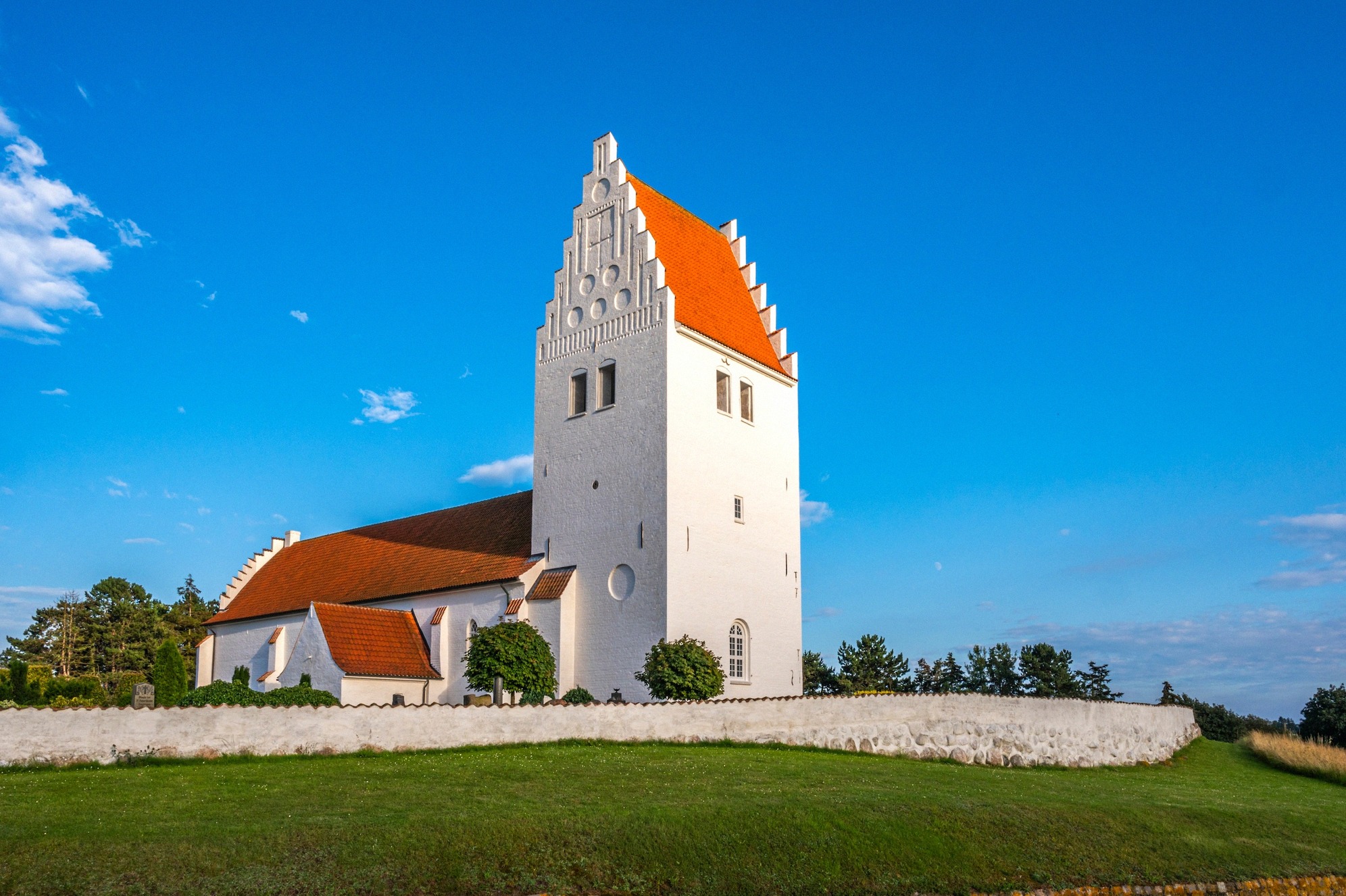 The white Fanefjord Kirke with orange roof and Gothic tower in a green field