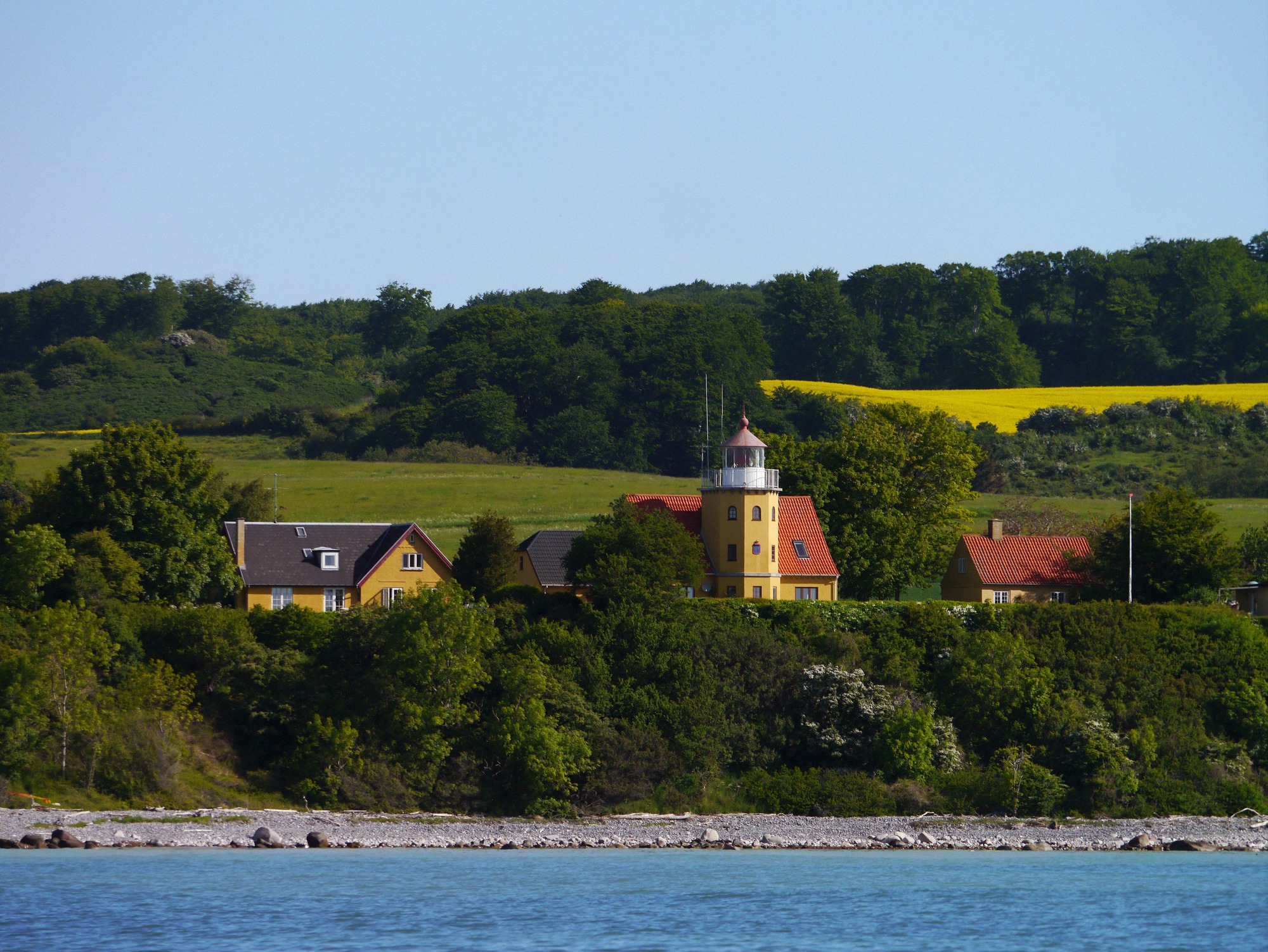 Møns Fyr above the coast, seen from the water. Møns Fyr above the green coastal landscape, seen from the water