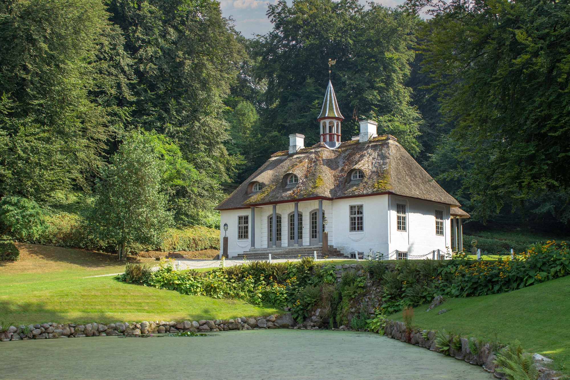 Das charmante Gärtnerhaus mit Strohdach im Liselund-Park zeigt die romantische Parklandschaft des dänischen Schlossgeländes.